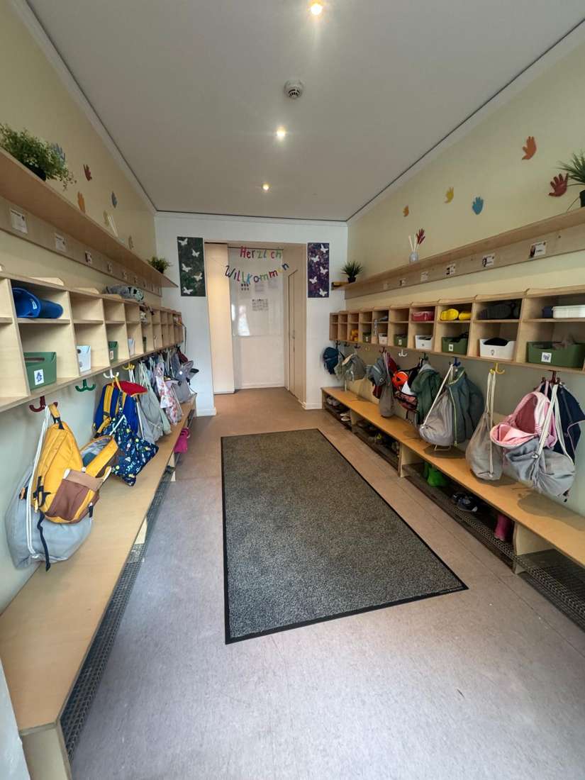 Die Garderobe unserer Kita mit bunten Rucksäcken und einem Herzlich-Willkommen-Schriftzug
