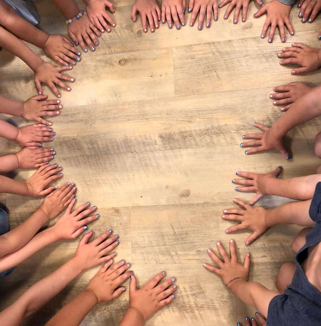 Kinderhände bilden gemeinsam einen Kreis auf dem Holzboden