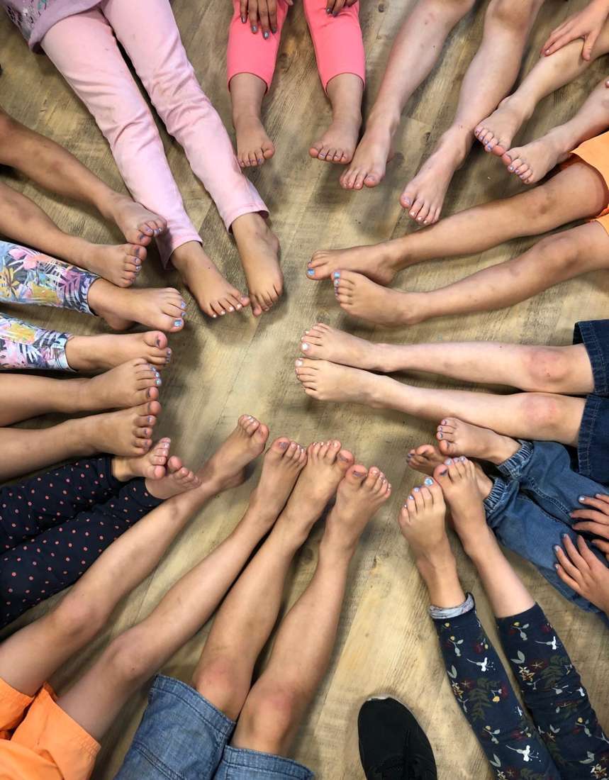 Kinderfüße bilden gemeinsam einen Kreis auf dem Holzboden