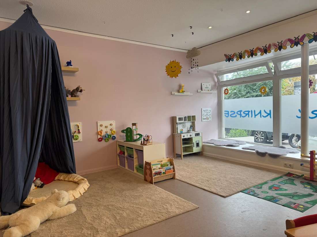 Heller Krippenraum mit Kuschelecke, Spielküche und großen Fenstern